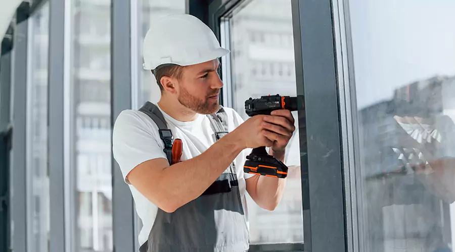 Construction worker installing modern glass door with drill